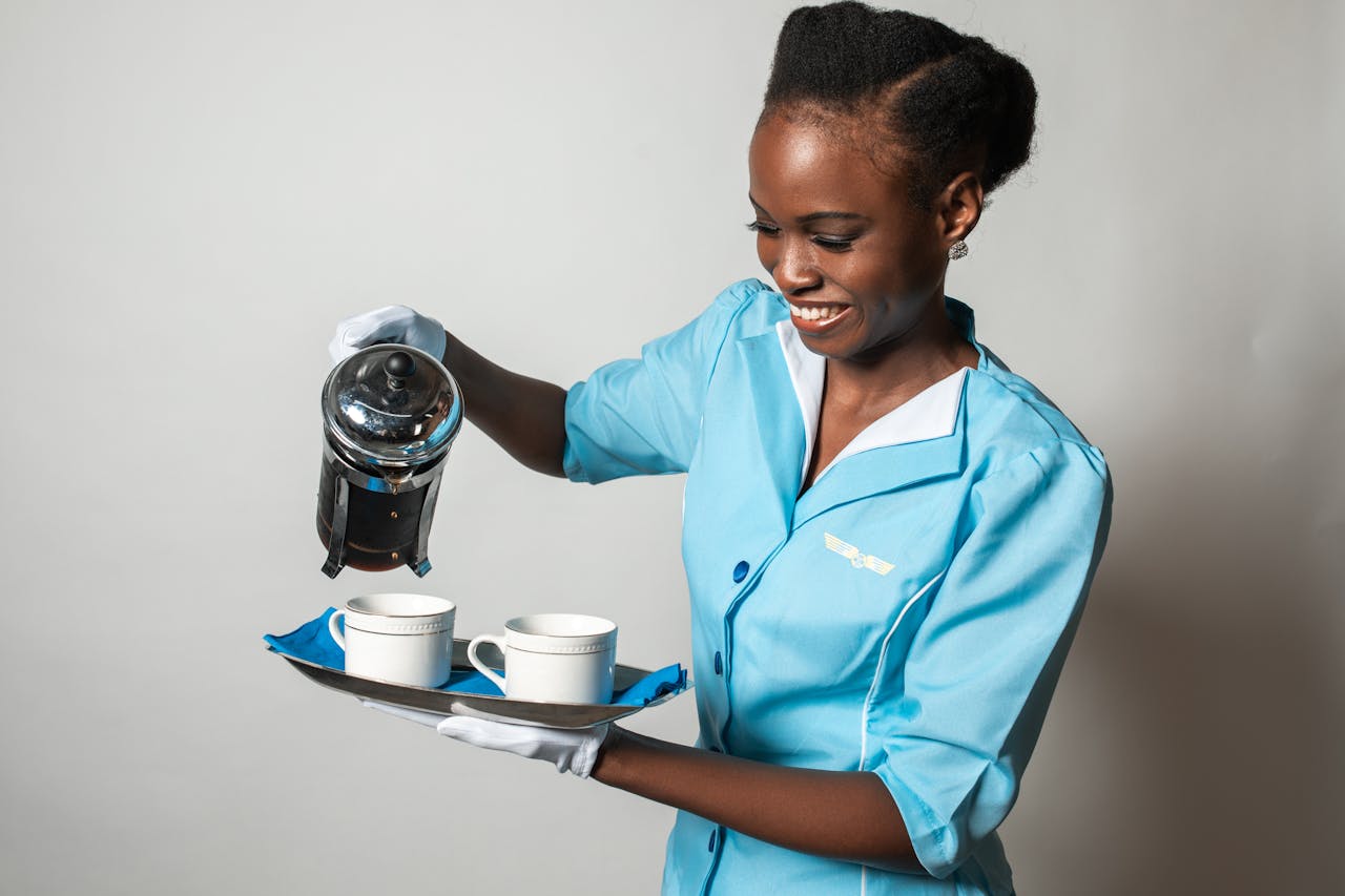 A cheerful flight attendant in a blue uniform pouring coffee with a French press.