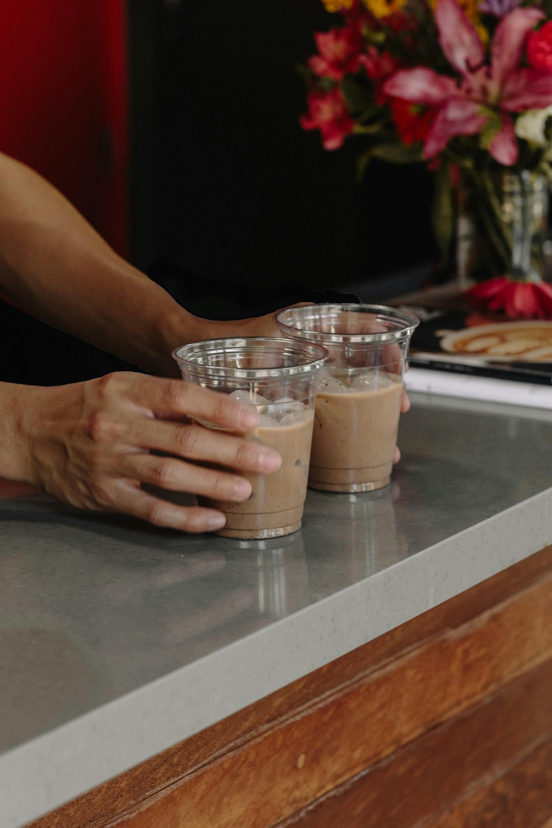 hands-holding-two-iced-coffee-drinks-on-counter-yvvwfmh0vsa